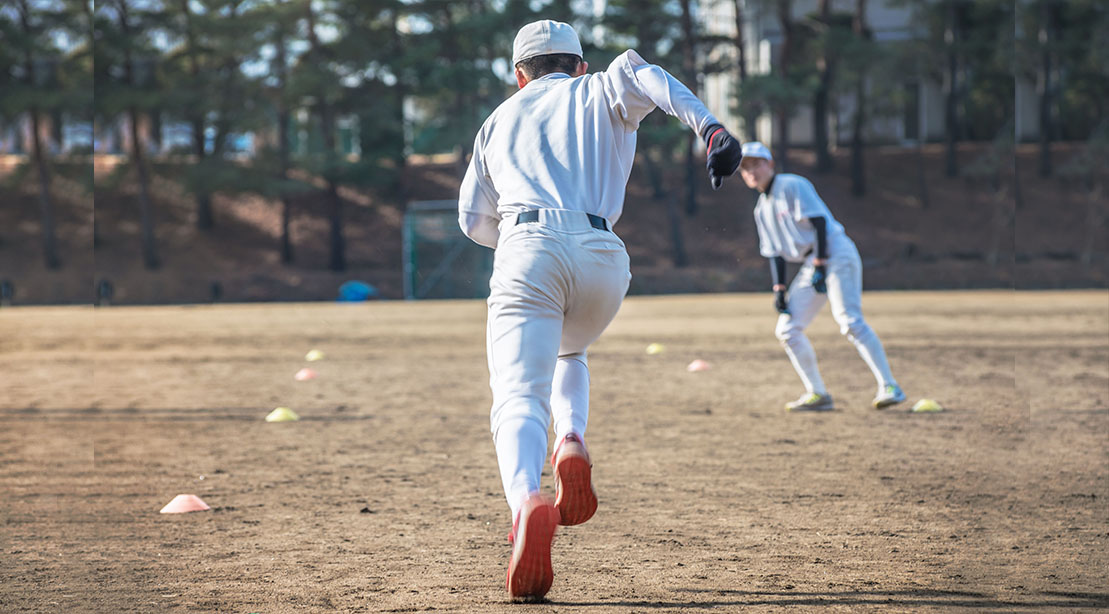 Baseball player taking in sprint training tips from his coach while practicing