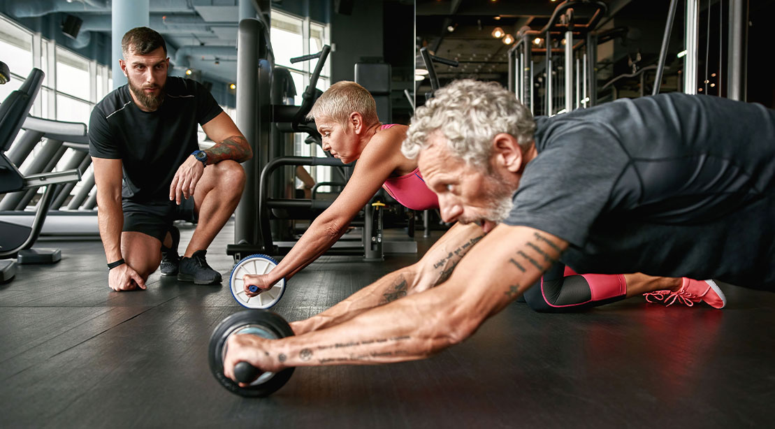 Elderly couple looking to become a super ager performing an ab rollout workout with a trainer