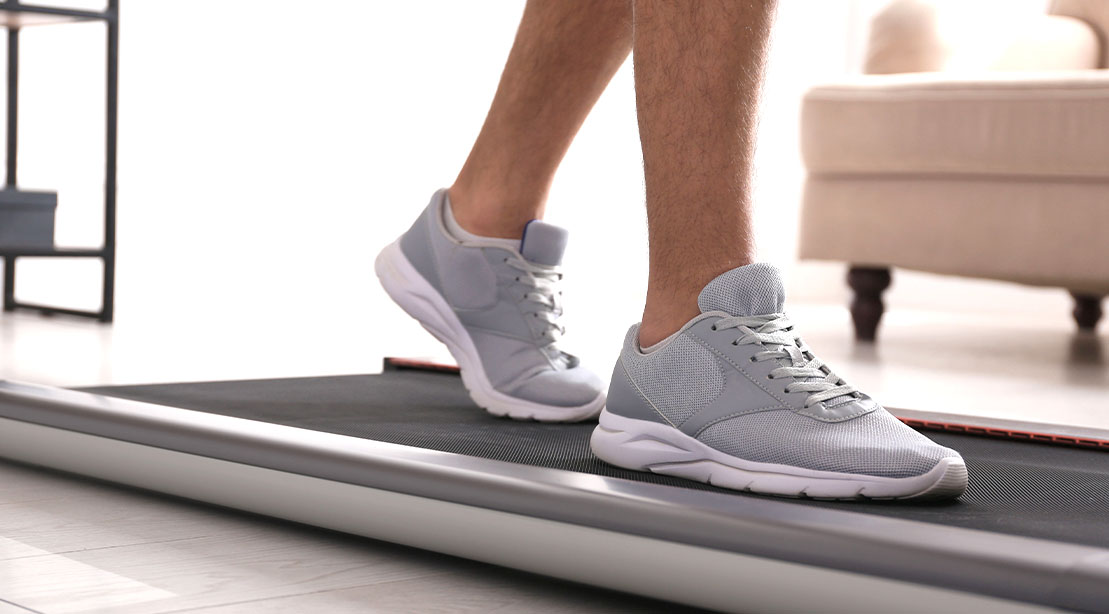 Fit man fixing his sedentary lifestyle at the office by using a walking pad