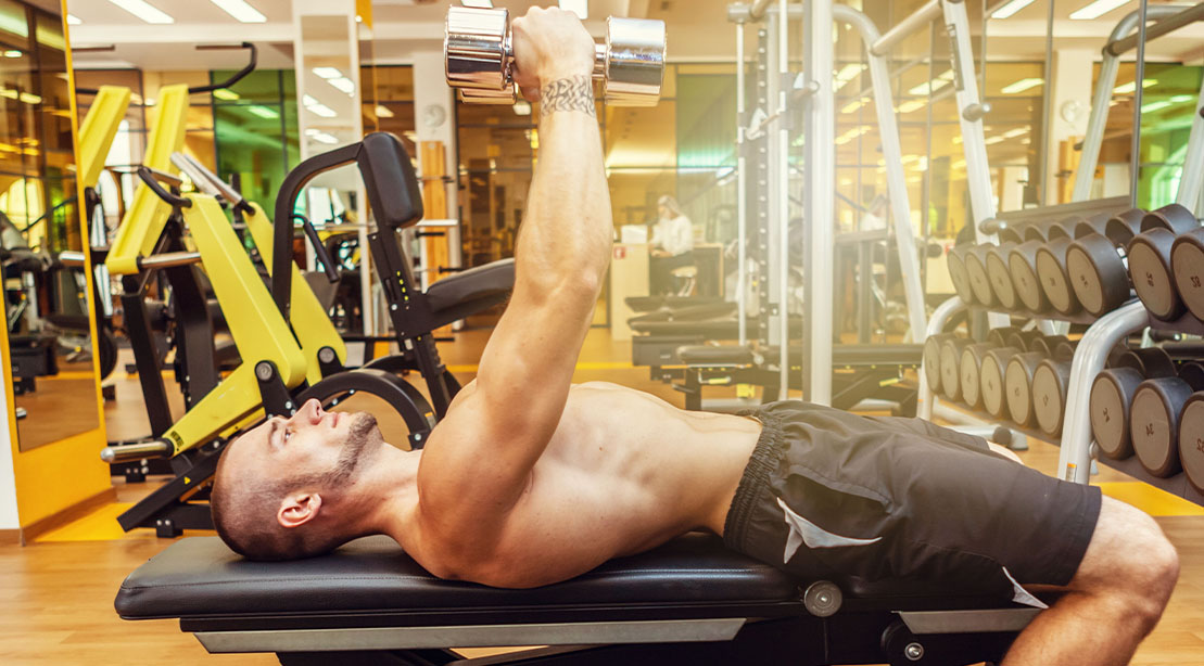 Fit muscular man performing a dumbbell squeeze press at the gym