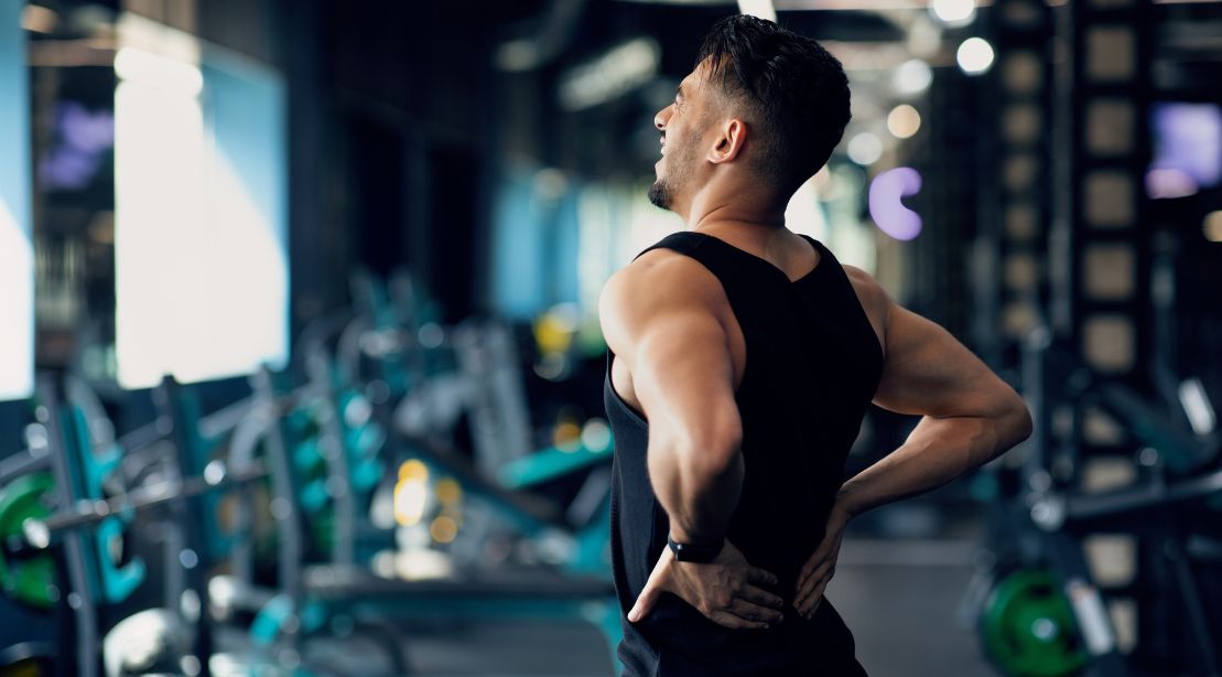 Young man holding his lower back in pain after lifting weights at the gym