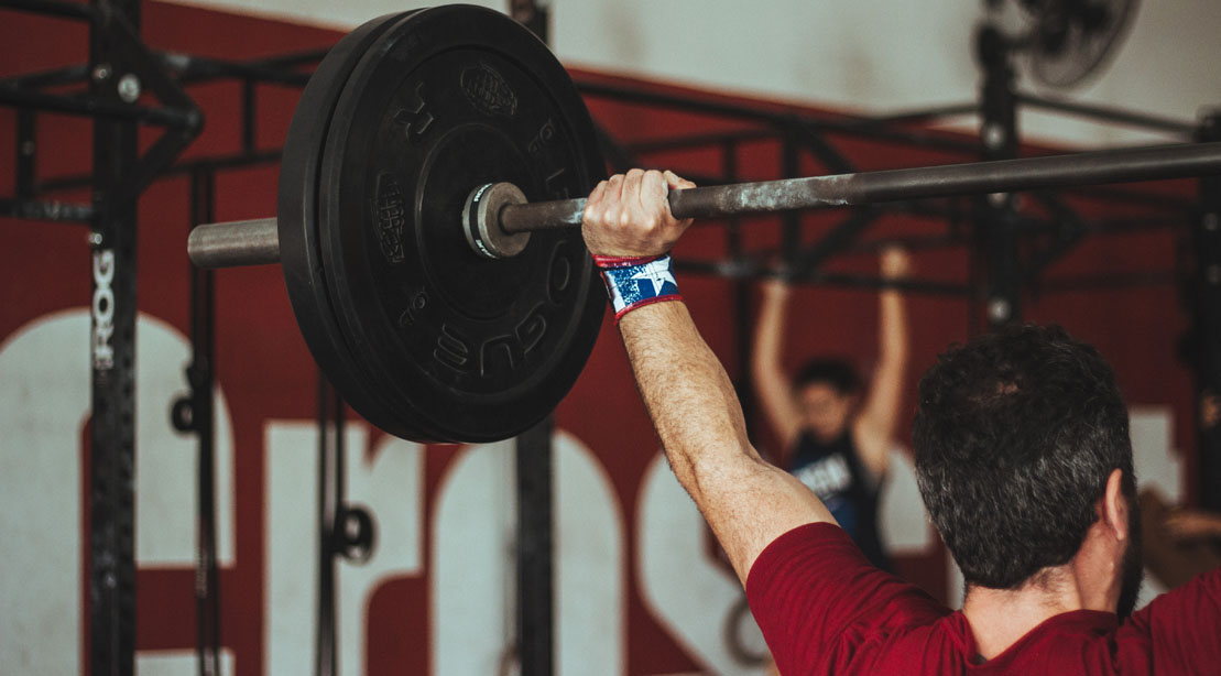 Man performing a full body workout with the barbell overhead carry exercise and overhead press accessory exercises