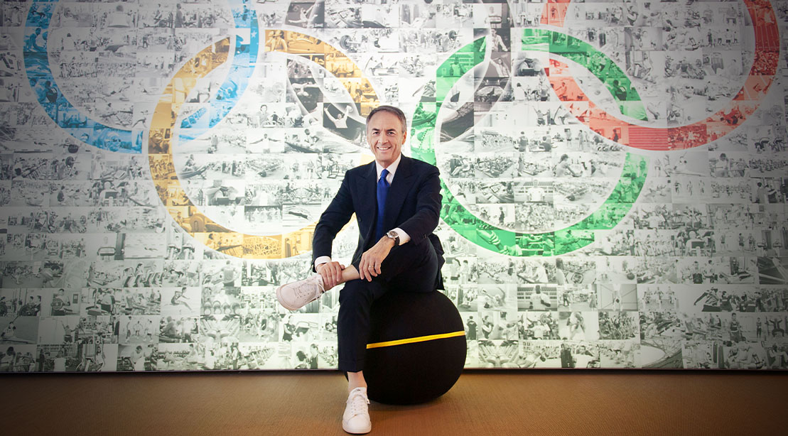 Newio Alessandri founder of technogym in front of a brick wall show casing the olympic rings