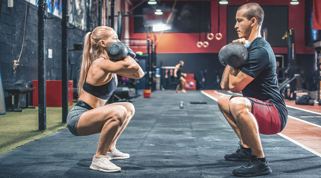 Training partners performing double kettlebell squats