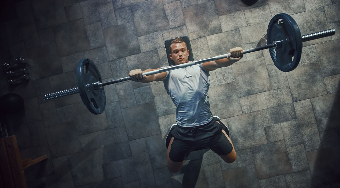 Young fit man performing a barbell bench press exercise while incorporating a cluster drop sets training method